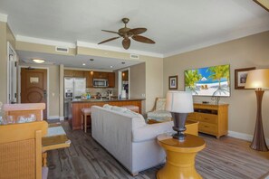 A living room with a sofa, a coffee table, a TV, and a kitchen in the background.