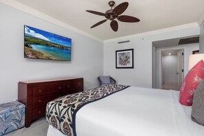 Un dormitorio con una cama, un aparador, un ventilador de techo, un cuadro enmarcado y una puerta.