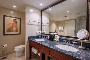 Un baño de hotel con dos lavamanos, un espejo grande, una obra de arte enmarcada en la pared y un inodoro.