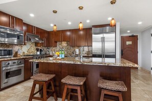 Una cocina moderna con electrodomésticos de acero inoxidable, encimeras de granito y taburetes de bar de madera.