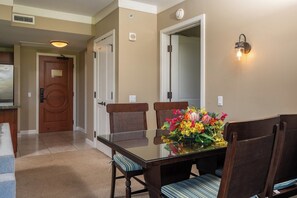 Un comedor con una mesa de vidrio, sillas acolchadas, un centro de mesa floral y una lámpara de pared.