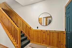 Una escalera de madera con barandilla, un espejo redondo en la pared y una puerta azul.