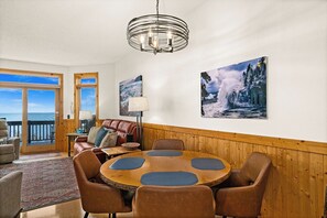 Una habitación con una mesa redonda de madera, sillas de cuero, una araña y un ventanal con vistas.