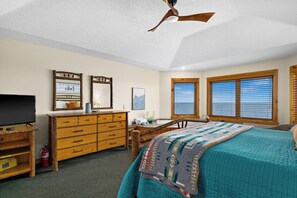 Un dormitorio con cama, cómoda, televisor y ventanas.