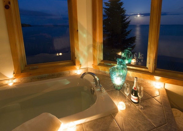 A bathroom with a bathtub, a glass vase, and a bottle of wine on the counter.