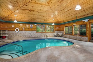 Una piscina interior con techo de madera, ventanas de vidrio transparente y una silla para salvavidas.