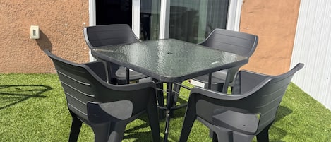 Un patio con una mesa y cuatro sillas, una puerta corrediza de vidrio y una lámpara fijada a la pared.