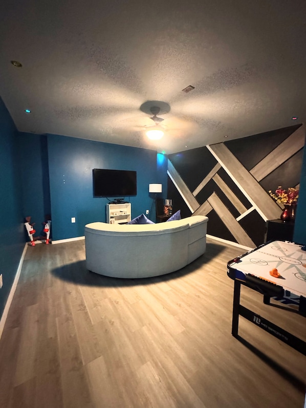 A room with a curved seating area, a flat-screen TV mounted on the wall, and a ceiling fan.