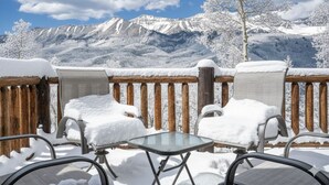 Un espace extérieur aménagé avec des sièges, recouvert de neige, et offrant une vue sur des montagnes aux sommets enneigés.