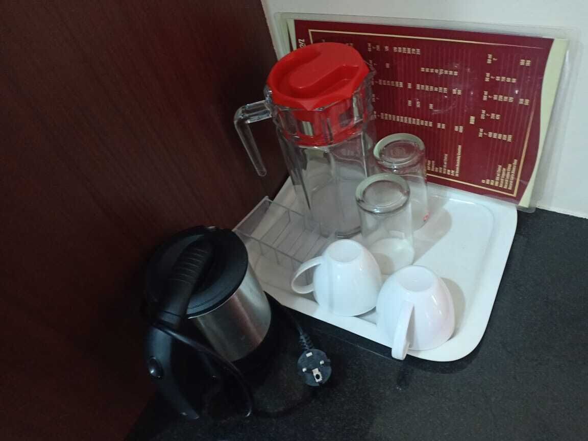 A coffee maker, a glass carafe, and several white cups on a tray.