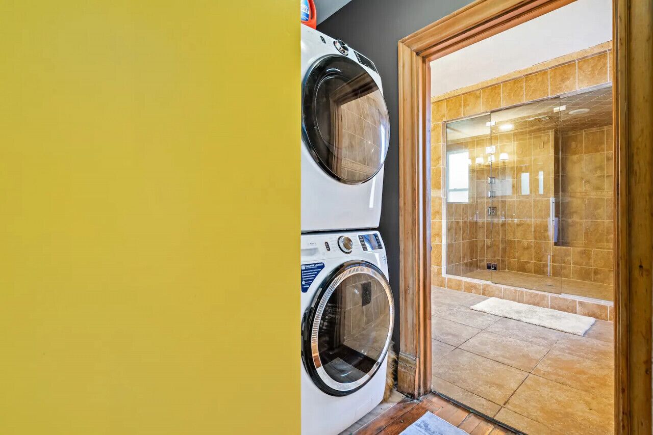 A laundry area with stacked washers and dryers, a shower with tiled walls, and a wooden door.