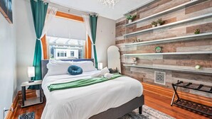 Un dormitorio moderno con cama, mesita de noche, estante montado en la pared con objetos decorativos y vistas al exterior.