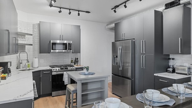 A modern kitchen with stainless steel appliances, a central island, and a dining area set for six. - PFR Suites - Highland, 3BR 2BA Shadyside Condo, 2 Decks and Off-Street Parking (Pittsburgh)