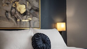 A bed with white linens and a dark, textured pillow. A painting with abstract elements is visible on the wall behind the bed. - Immaculate Double King Suite| 2 Decks| A+ Location (Pittsburgh)