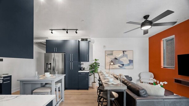 A modern kitchen with dark cabinets, a central island, and a dining area with a long table and bar stools.