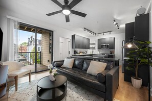A modern living room with a black leather sofa, a round coffee table, and a view of the city through large windows.