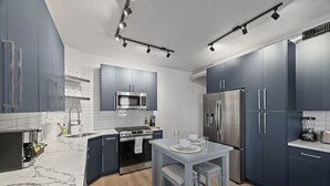 A modern kitchen with dark blue cabinets, a stainless steel refrigerator, a microwave, and a built-in oven.