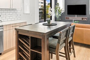 A modern kitchen with a wooden table and chairs, a built-in wine rack, and a flat-screen TV mounted on the wall.