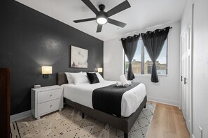 A modern bedroom with a bed, bedside tables, a ceiling fan, and a window with curtains.