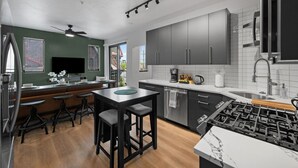 A modern kitchen with dark cabinets, a central island, bar stools, and a built-in stove. - Stunning 3BR suite| 2 private decks| A+ Location! (Pittsburgh)