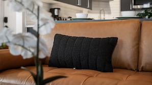 A modern kitchen with dark cabinets, a stainless steel oven, and a dining area with a brown leather sofa and a black cushion. - Stunning 3BR Penthouse Suite| 2 decks| A+ Location (Pittsburgh)