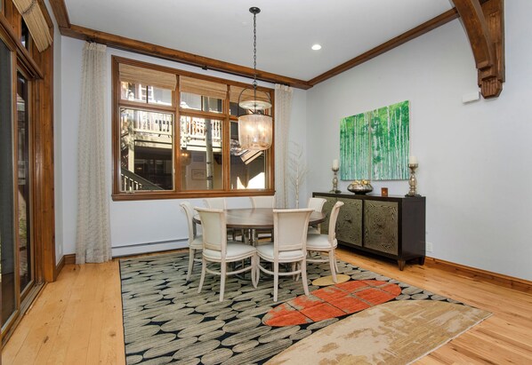 A dining area with a wooden table and chairs, a patterned rug, and a large window with a view of buildings.