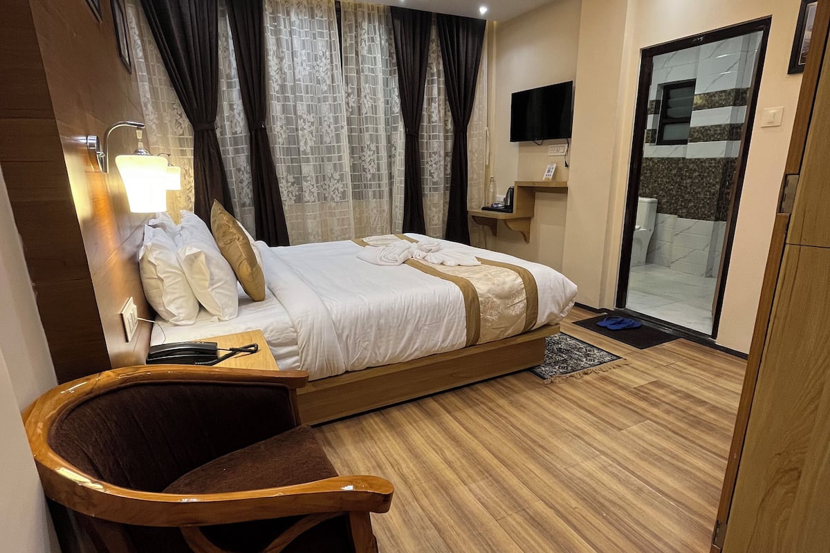 Moderni hotellihuone, jossa on sänky, yöpöytä, lamppu, verhot ja televisio.