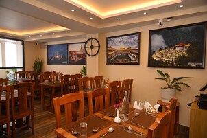 A restaurant with wooden tables and chairs, framed pictures on the walls, and a ceiling with recessed lighting.