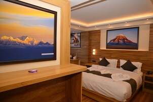 Una habitación de hotel con una cama grande, un escritorio de madera y dos grandes cuadros enmarcados de montañas.