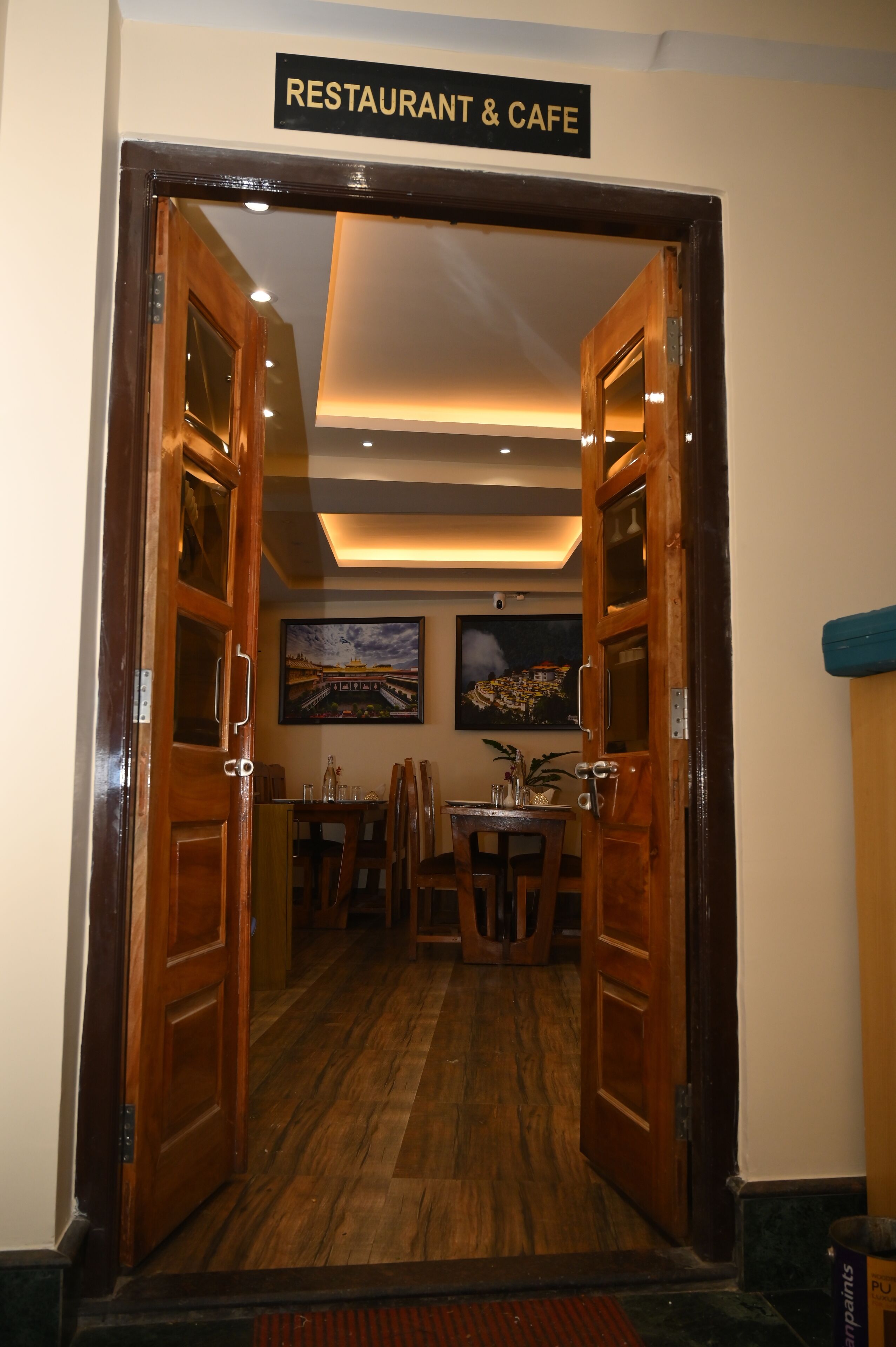 A restaurant entrance with wooden doors, a dining area with tables and chairs, and a ceiling light fixture.