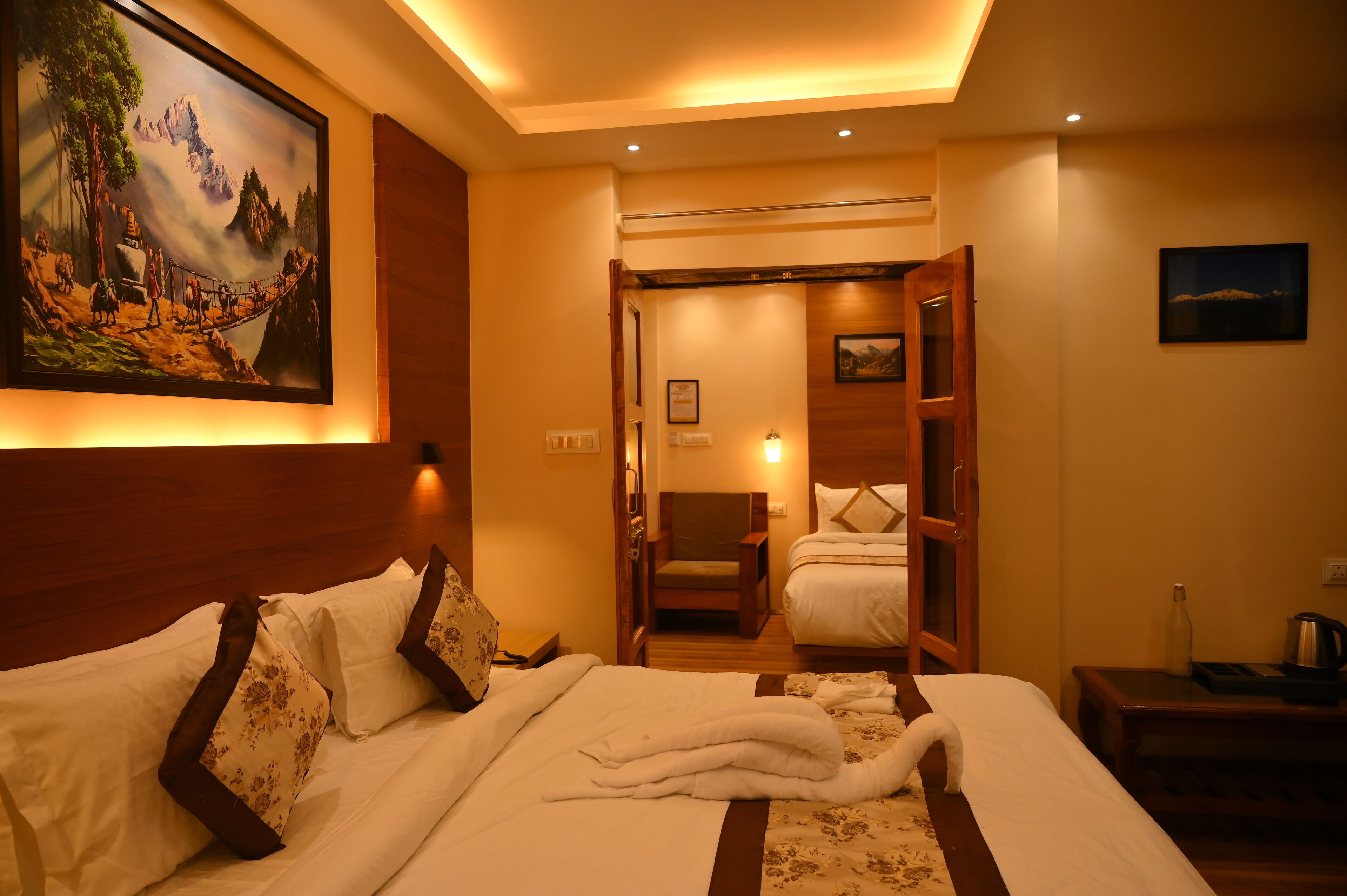 A hotel room with a large bed, a painting on the wall, a wooden headboard, and a nightstand with a lamp.