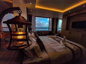 Quarto de hotel com uma cama grande, uma mesa de cabeceira, um abajur e vista do céu pela janela.