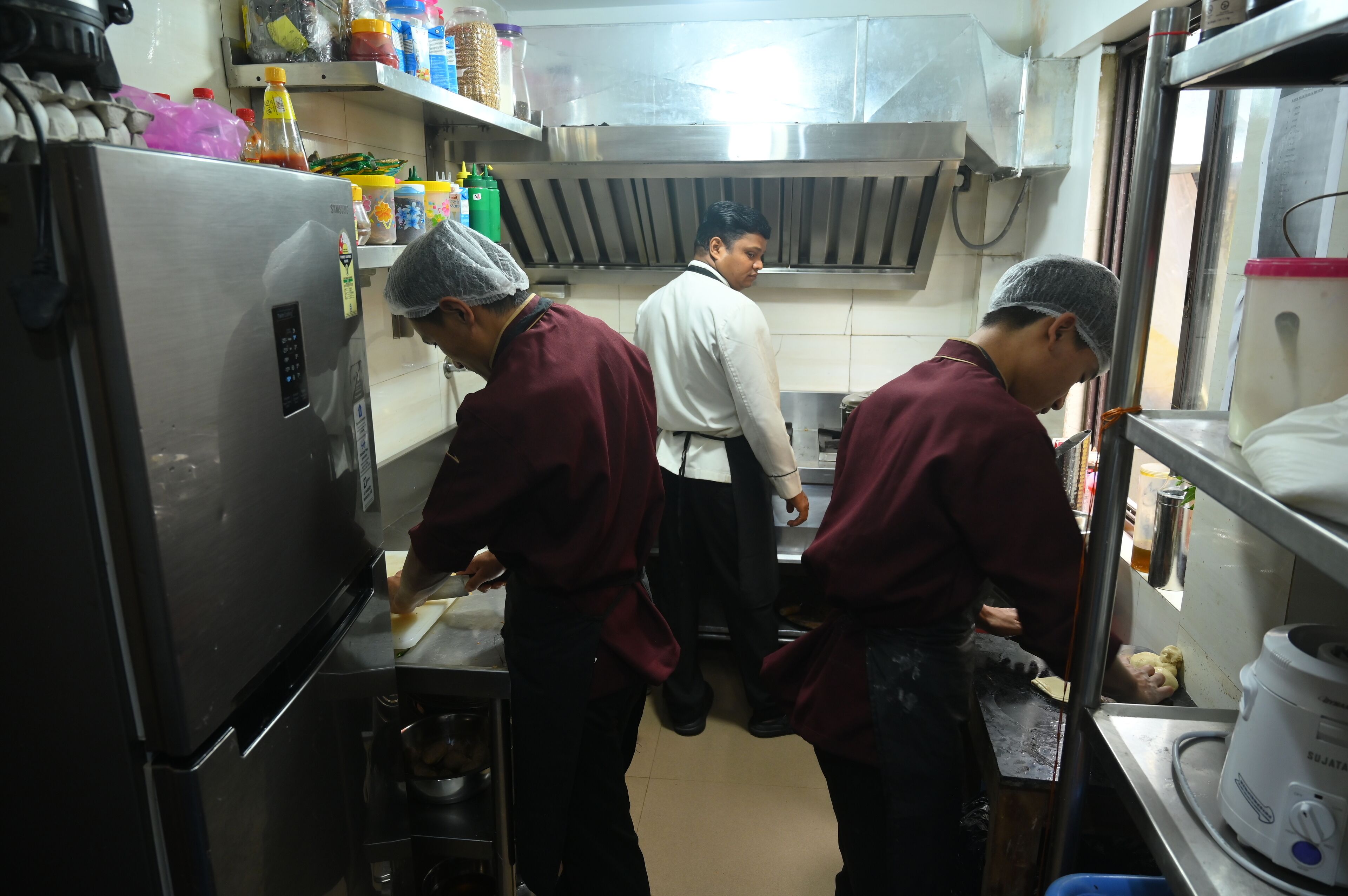 Cocina comercial con electrodomésticos de acero inoxidable, incluyendo un refrigerador y un procesador de alimentos.