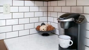 Eine Küche mit weiß gefliestem Spritzschutz, Holzschränken, einer Kaffeemaschine und einer Schüssel Obst.