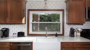 Eine Küche mit Holdelementen, einer weißen Arbeitsplatte, einem Fenster, einer Spüle, einem Toaster, einer Kaffeemaschine und einem Messerblock.