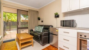 Ett kompakt bostadsutrymme med en soffa, ett litet träbord, en liten köksdel med mikrovågsugn och ugn samt en skjutdörr i glas som leder ut till ett utomhusområde.