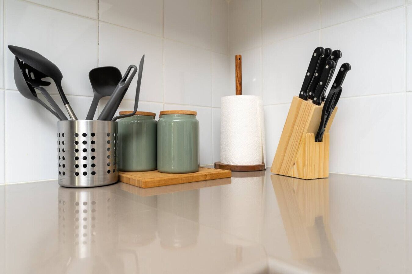 A kitchen counter with utensils, jars, and a paper towel holder.