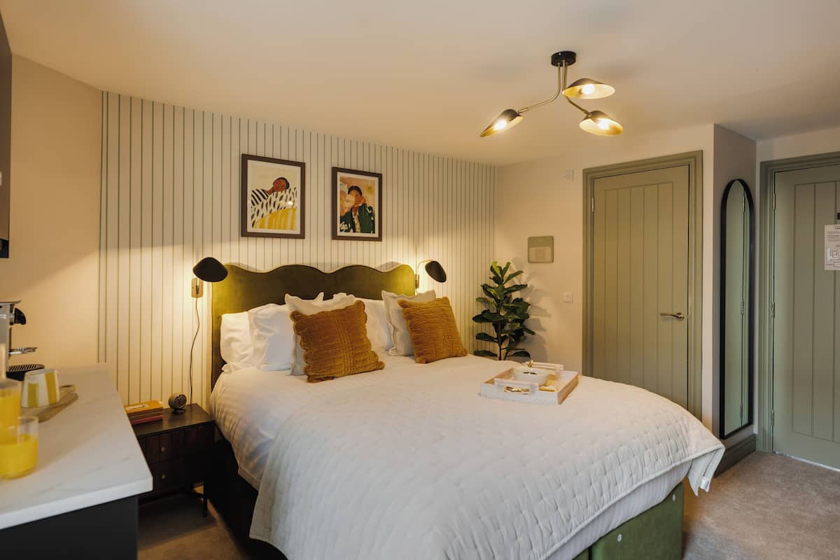 Un dormitorio ordenado con cama, mesita de noche, lámpara y cuadros en la pared.