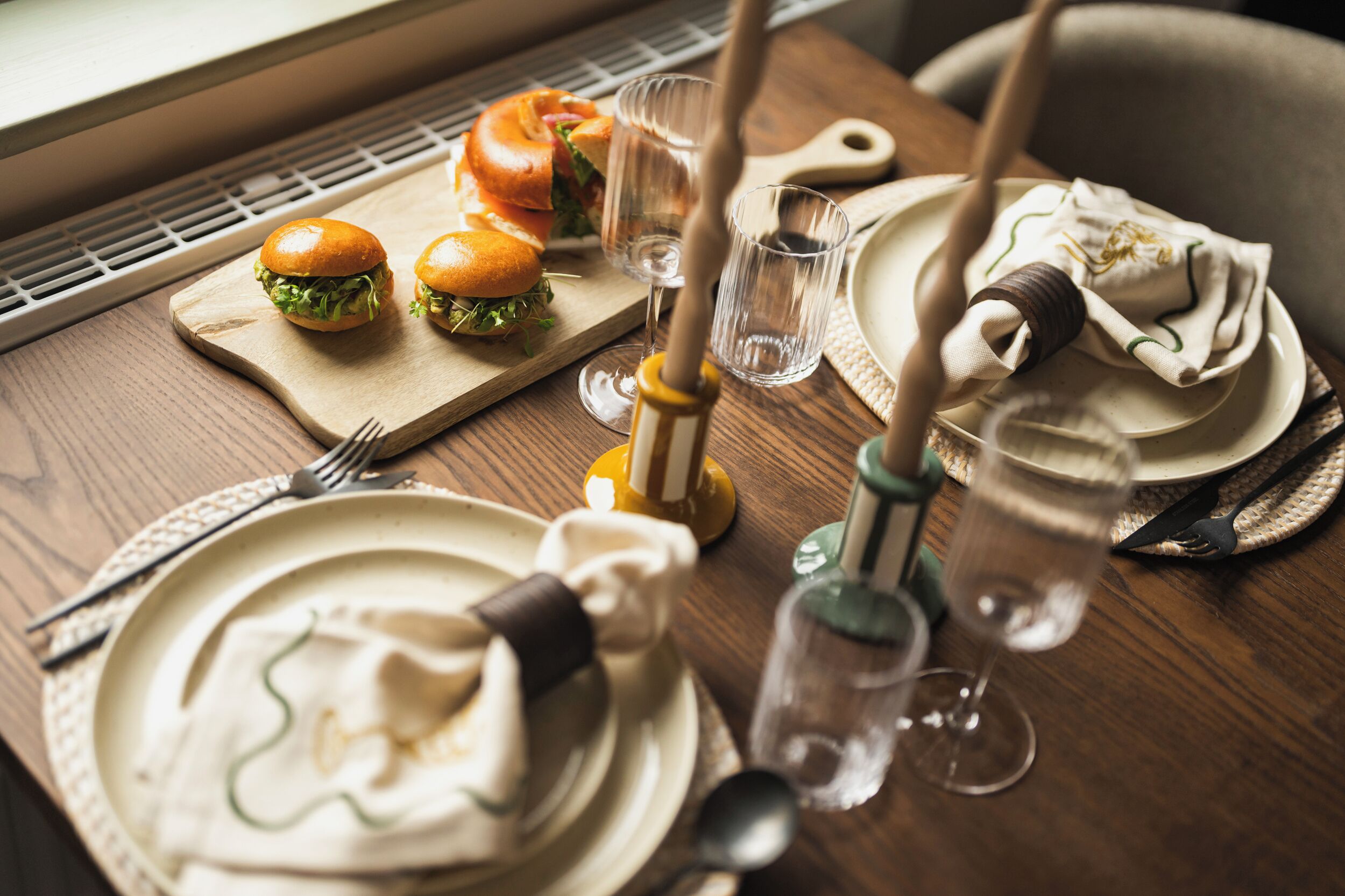 A dining table set with plates, cutlery, glasses, and a sandwich.