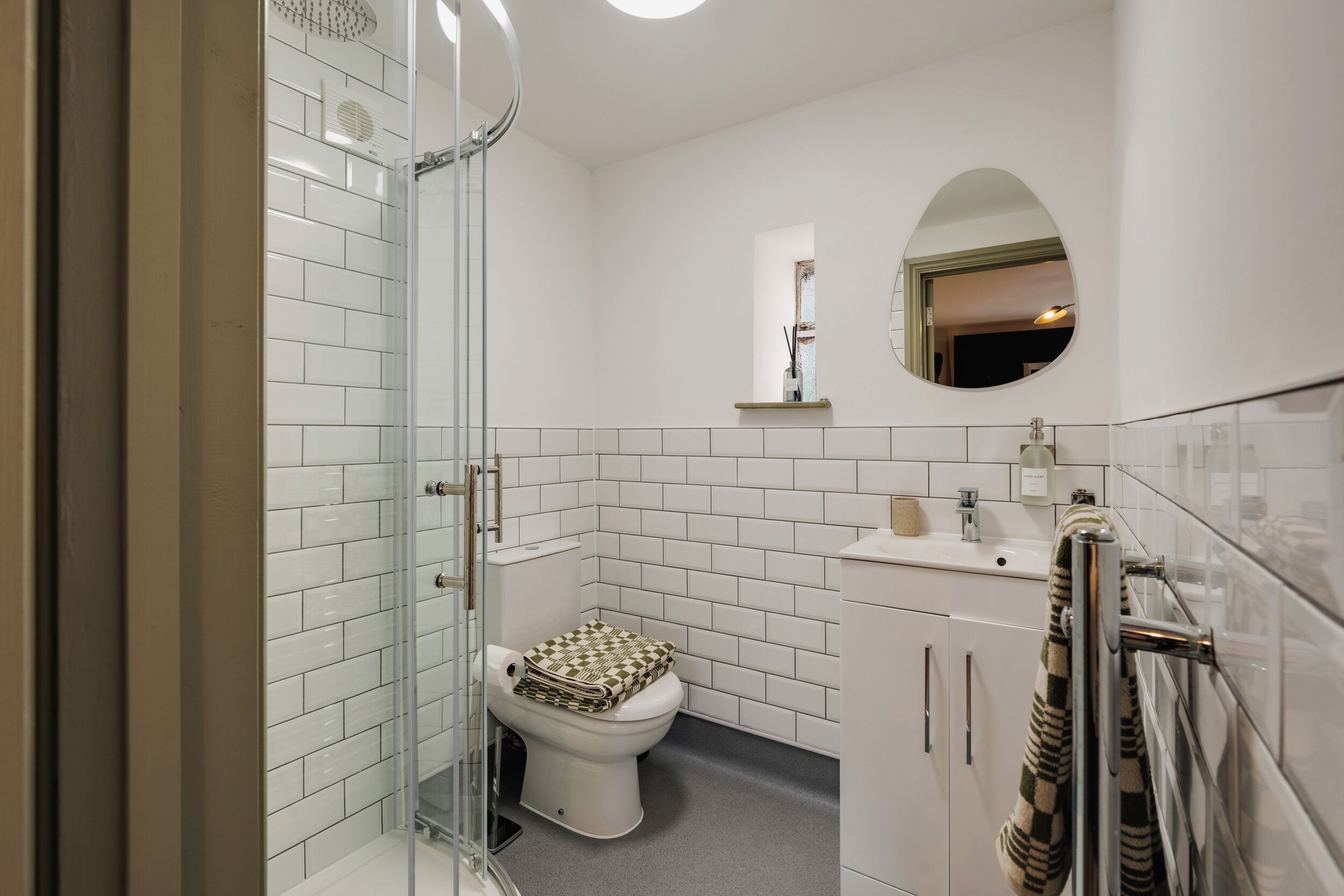 A modern bathroom with a glass shower enclosure, a toilet with a patterned seat cover, and a sink with a towel rack.