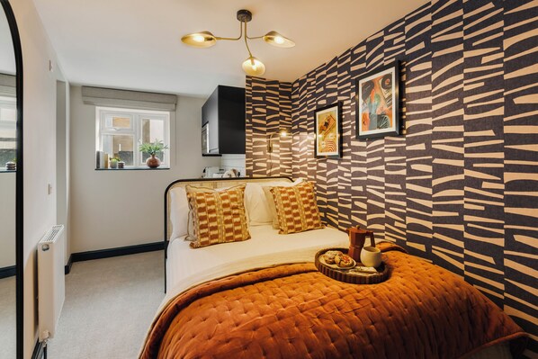 Un dormitorio con cama, ventana, radiador, luz de techo y pared con diseño.