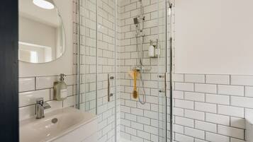 A modern bathroom with a glass-enclosed shower, white tiled walls, a sink with a mirror, and a soap dispenser.