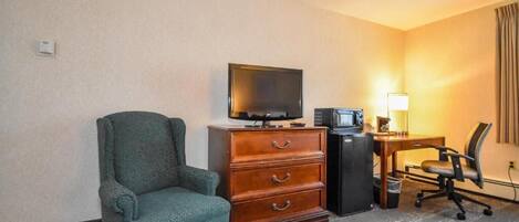 A hotel room with a green armchair, a wooden dresser, a television, a desk with a computer, and a lamp.