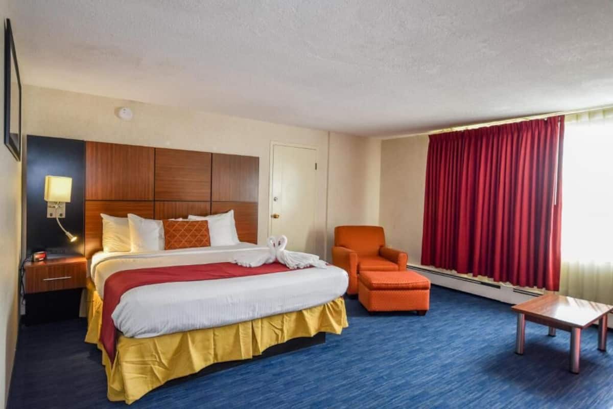 A hotel room with a bed, a chair, a table, and a window with curtains.