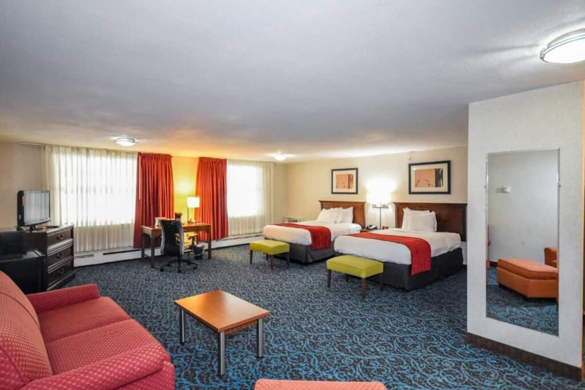 A hotel room with two beds, a desk, a chair, a TV, and a sofa.