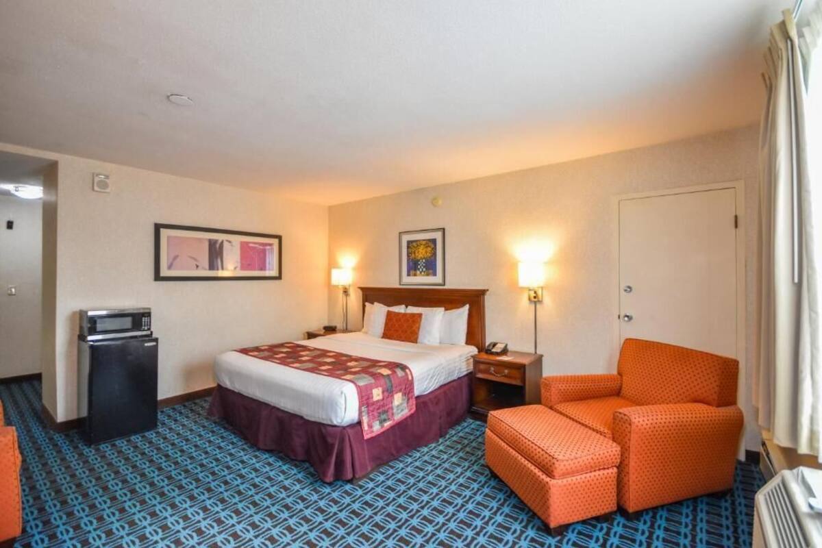 A hotel room with a bed, two bedside lamps, a chair, a desk, and a microwave.