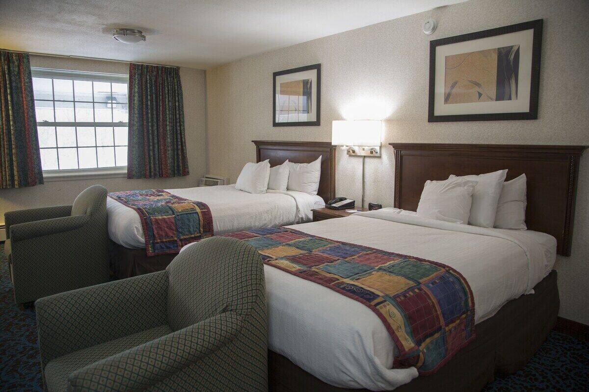 A hotel room with two beds, a chair, a window with curtains, and framed artwork on the walls.