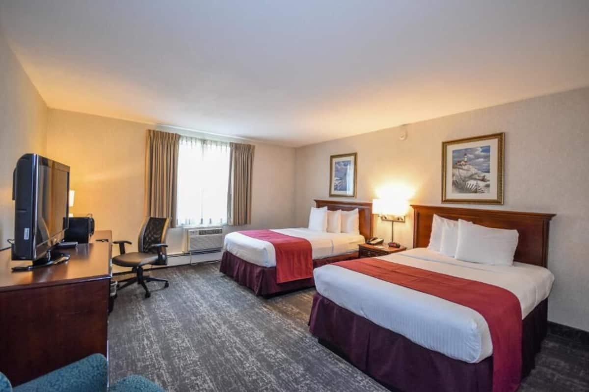 A hotel room with two beds, a desk with a computer, a chair, and a TV.