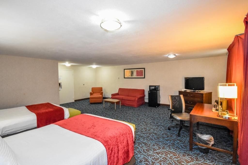 A hotel room with two beds, a desk with a lamp, a television, a chair, and a small table.