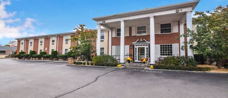 A two-story building with a central entrance flanked by columns, surrounded by a parking lot and greenery.